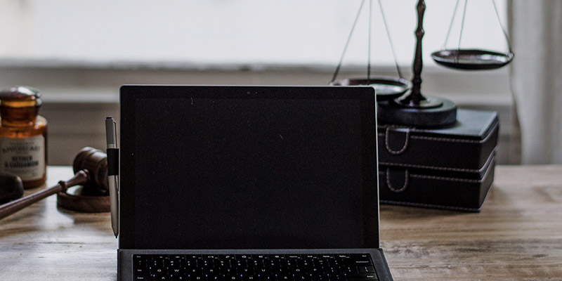 Laptop on a desk next to a gavel and scales of justice